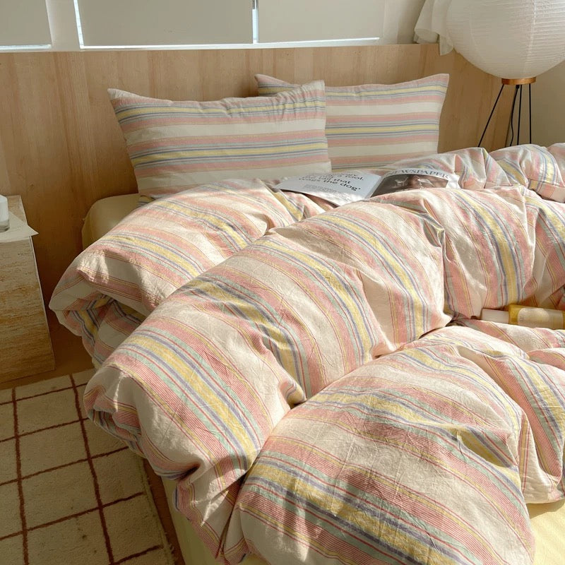 Bed with striped bedding in a room with wooden flooring and a lamp.