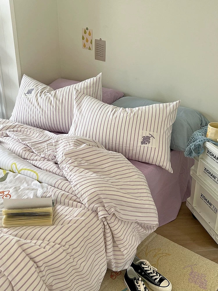 Purple applique duvet cover draped over a lilac sheet with striped pillows at the head of the bed.