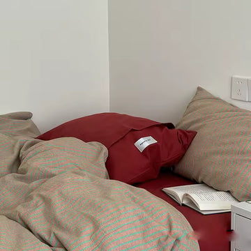 Red pillow on a bed with beige striped bedding and an open book.