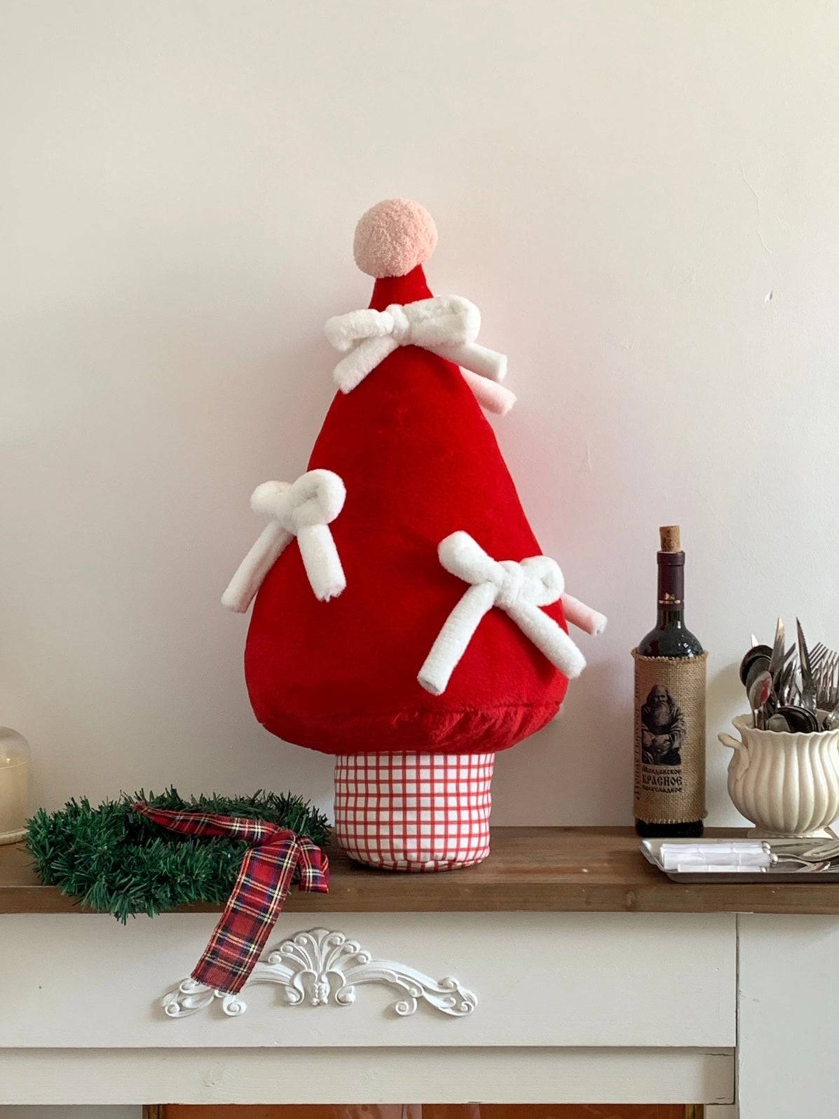 Red Christmas tree shaped pillow with white bows styled on a holiday shelf