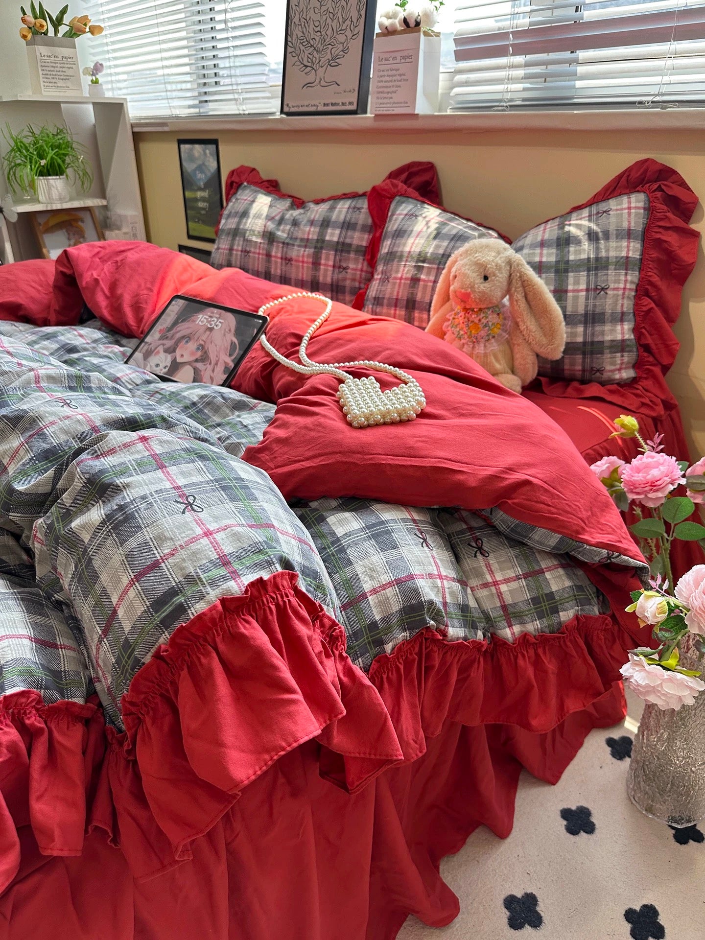 Bed with red and plaid bedding, teddy bear, and pink flowers.