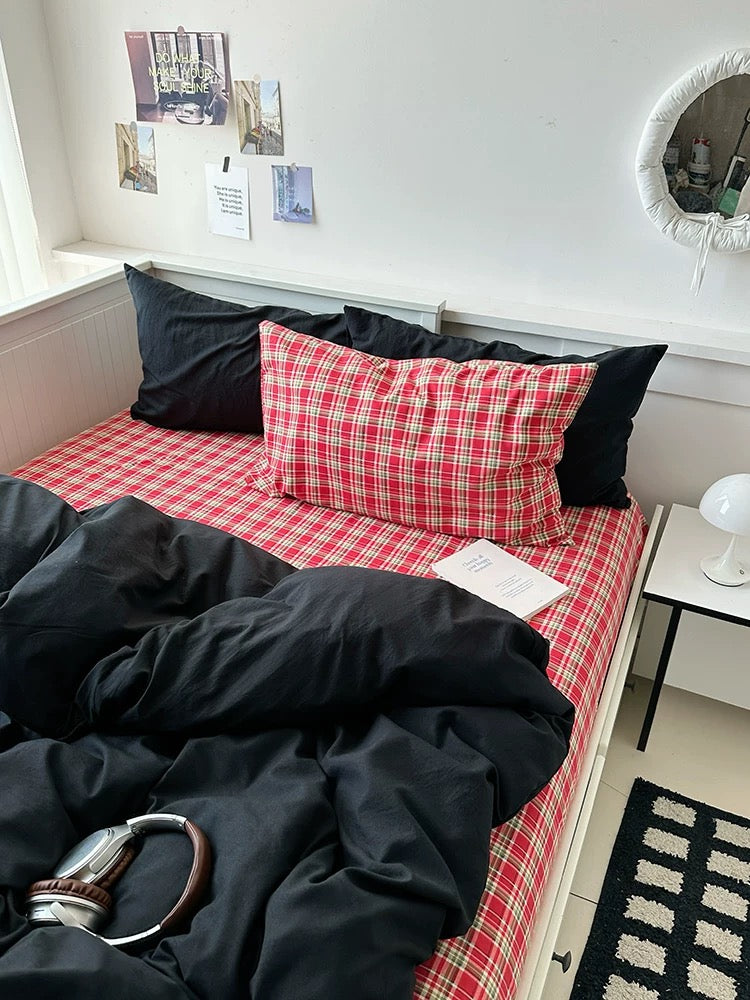 Bed with red checkered sheets and black pillows in a room with a mirror and small table.