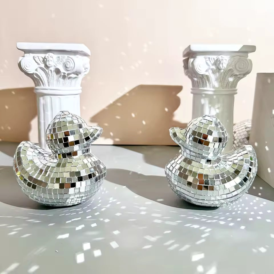Two silver disco duck decorations on a reflective surface with classical columns in the background.