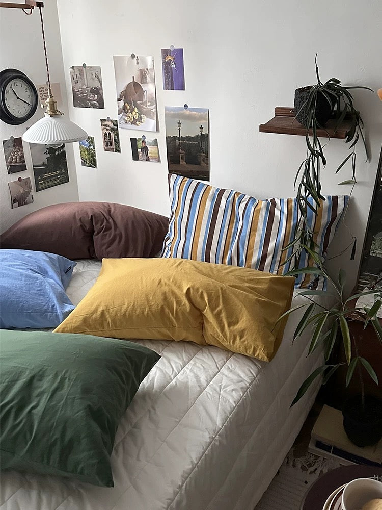 Mustard and pine green pillowcases sit in front of mocha and striped pillowcases.