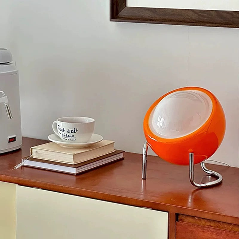 Orange and white spherical lamp on a wooden surface with books and a cup.