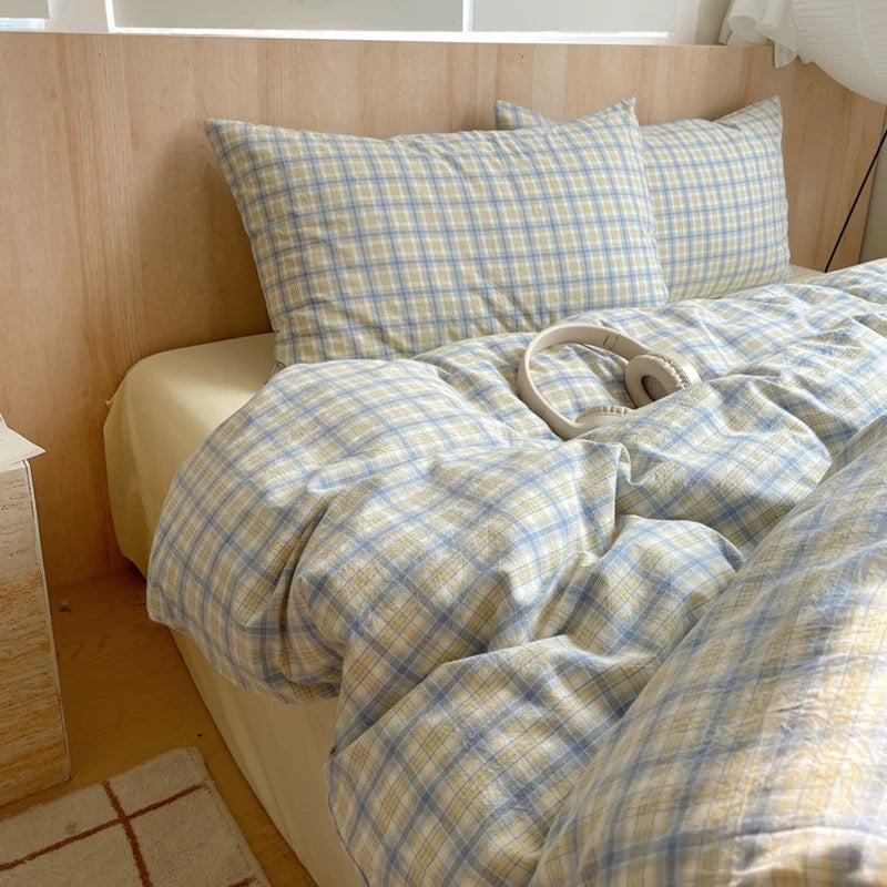 Bed with plaid bedding and pillows in a room with wooden headboard and floor.