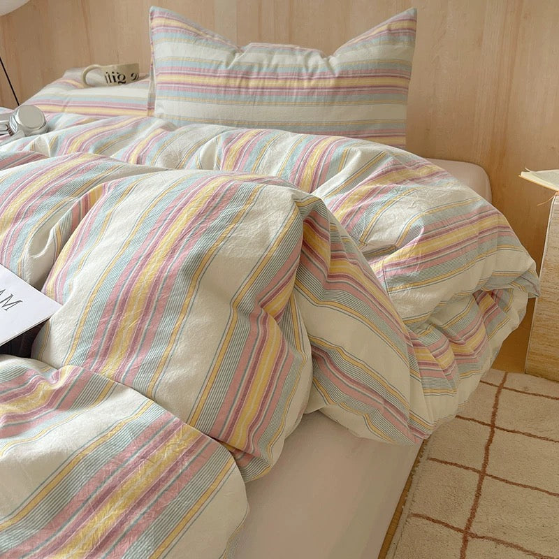 Striped bedding set on a bed with pillows and a lamp in the background.