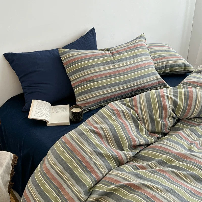 Two striped pillowcases stacked beside a navy pillow with an open book and ceramic mug