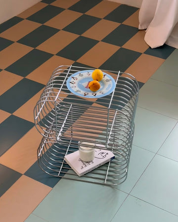 Metallic wire side table with a plate of fruit on a checkered floor.