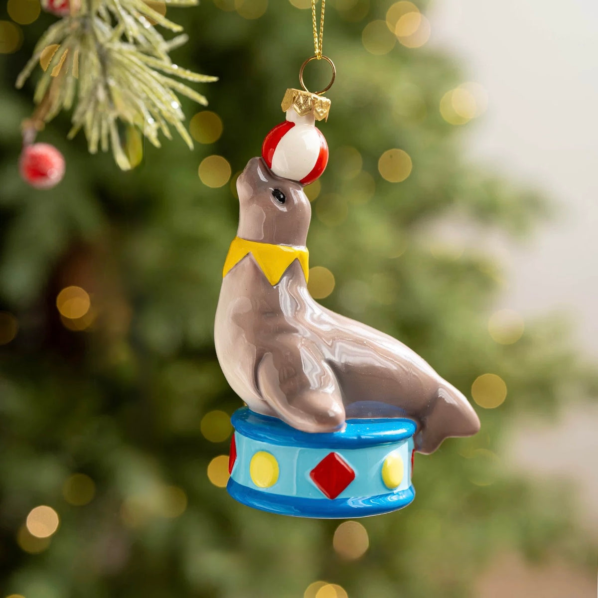 A seal ornament balances a red and white ball on its nose above a blue pedestal with red diamond details.