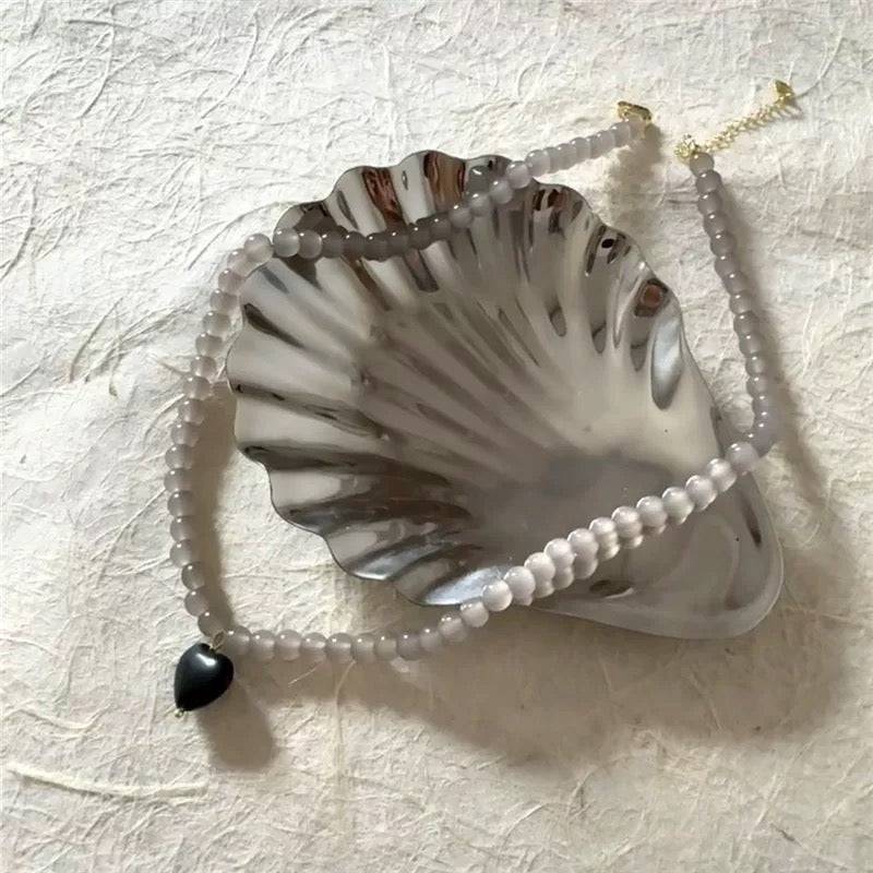 Pearl necklace with a black bead on a textured beige surface