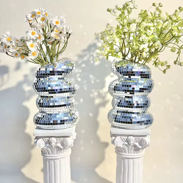 Two silver mosaic vases with floral arrangements on decorative columns against a light background
