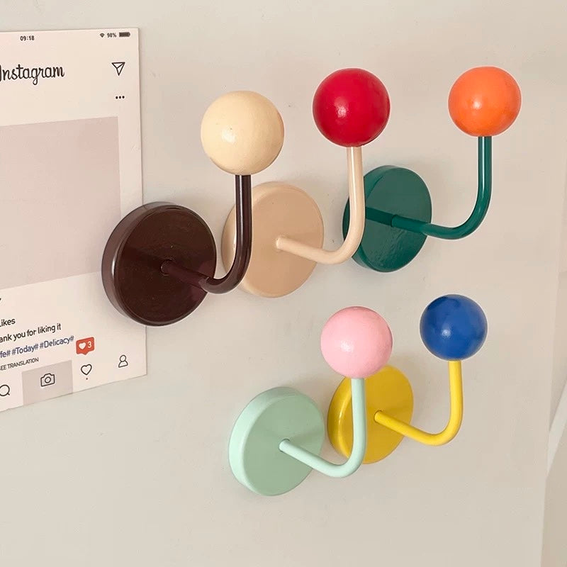 A set of six wall-mounted coat racks with round, colorful knobs and curved hooks, shown hanging on a white wall next to a printed Instagram post.