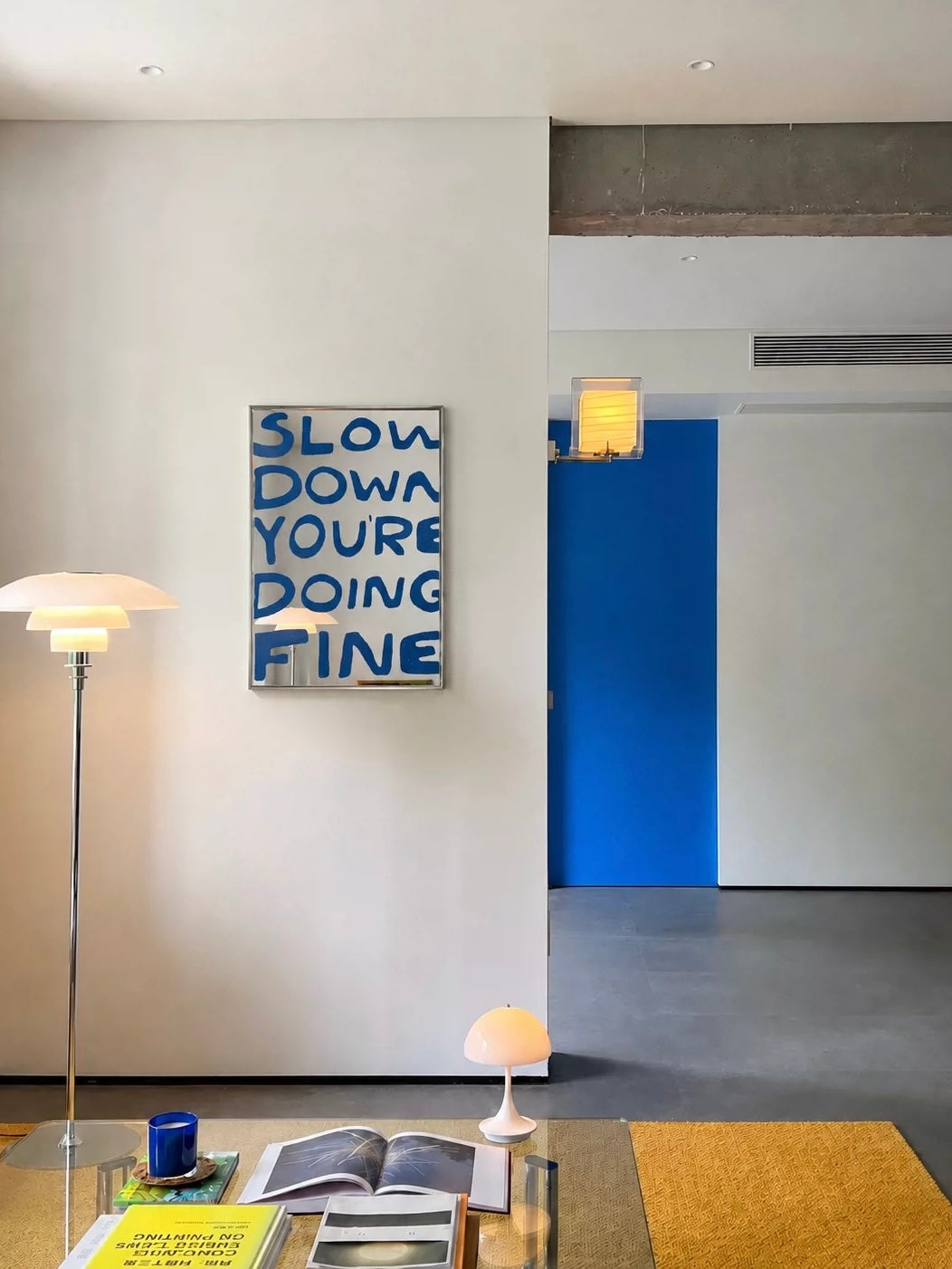 The Slow Down mirror hangs in a living room, with large blue letters stacked inside a slim silver frame.