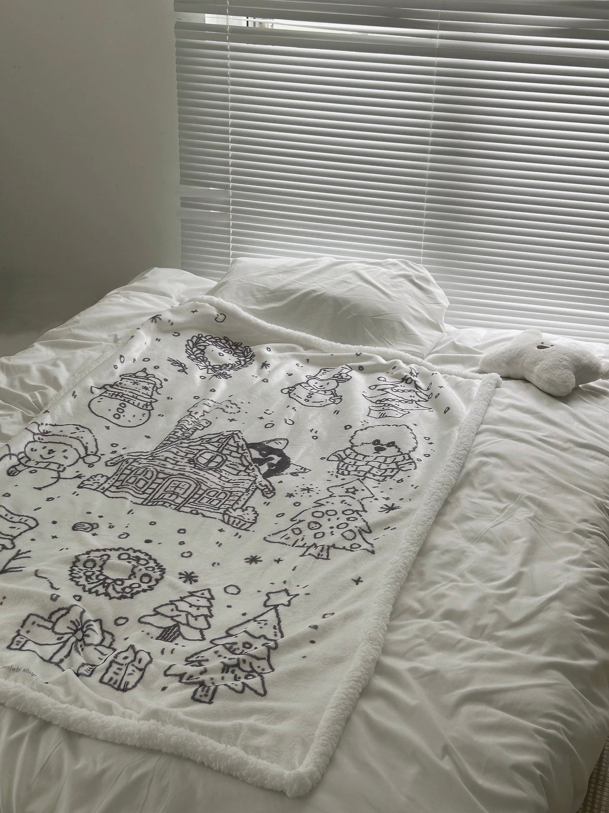 Snowy Christmas fleece throw blanket styled across white bedding in a bright bedroom