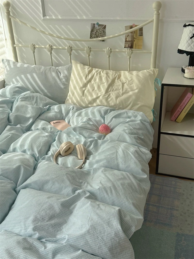 Bed with light blue bedding and white pillows, nightstand with books in the background