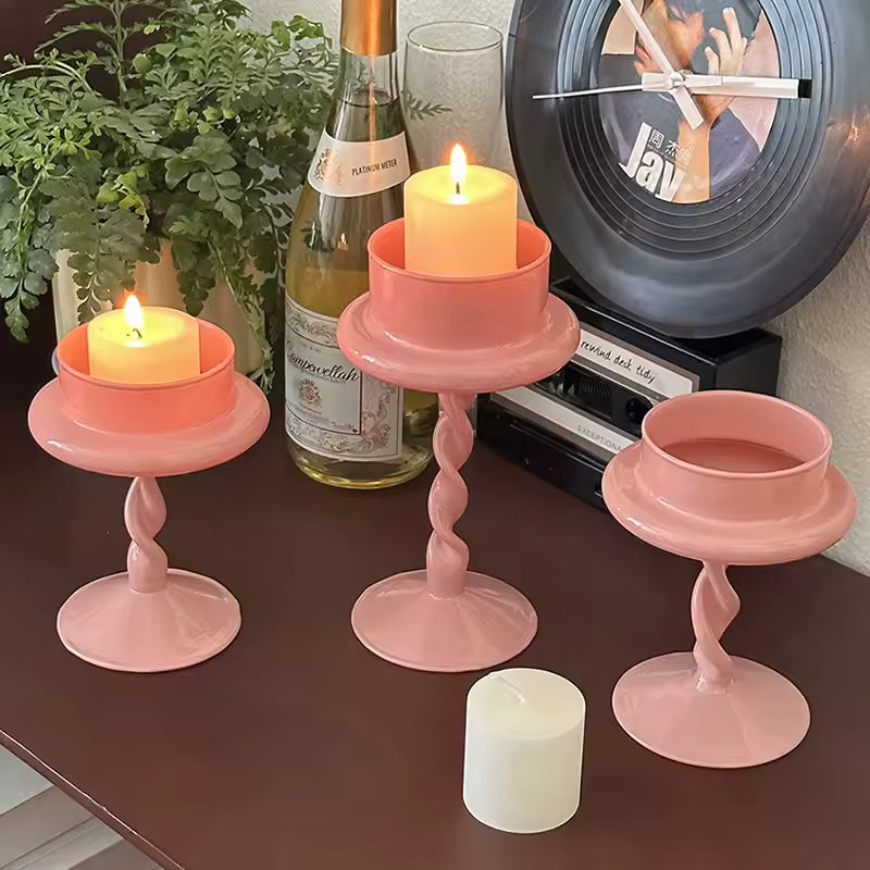 Two pink candle holders with candles on a table next to a person reading a book.