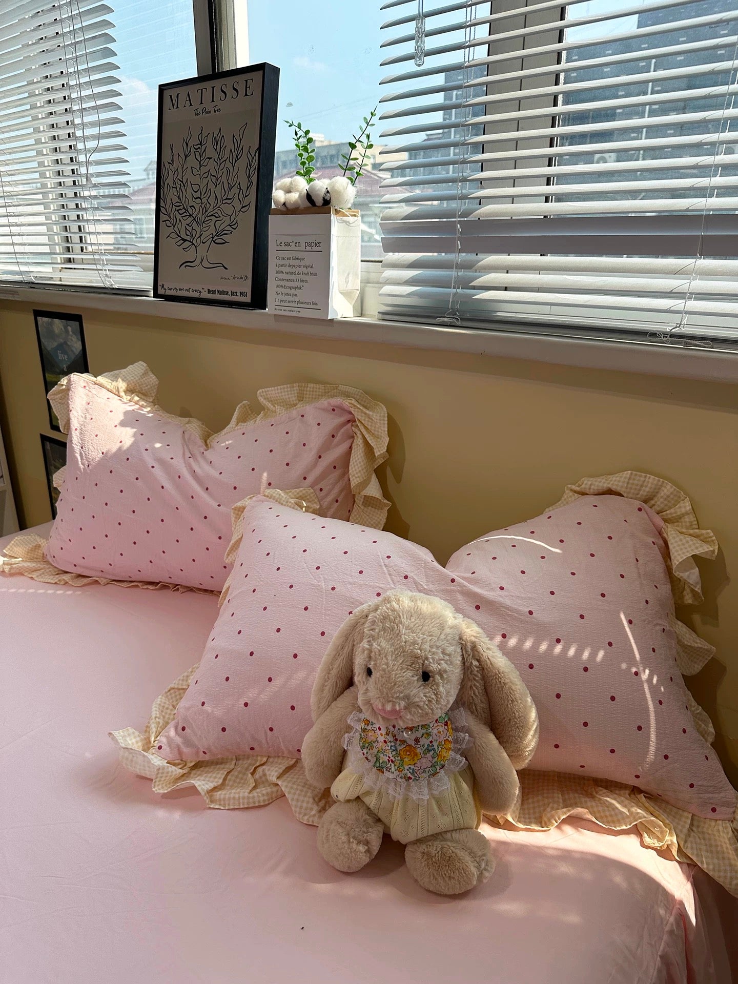 Pink polka dot pillows with a bunny toy on a bed near a window.