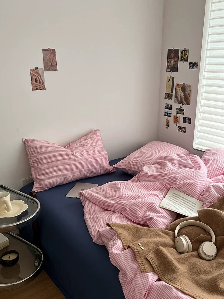 Bed with pink checkered bedding and pillows, next to a nightstand with a cup and saucer.