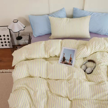 Yellow striped bedding on a bed with blue pillows and a lamp in the background.