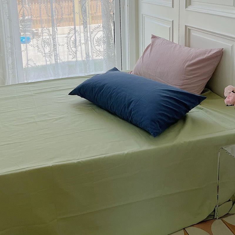 A grass-green sheet is paired with navy and pink pillows in a sunlit bedroom.