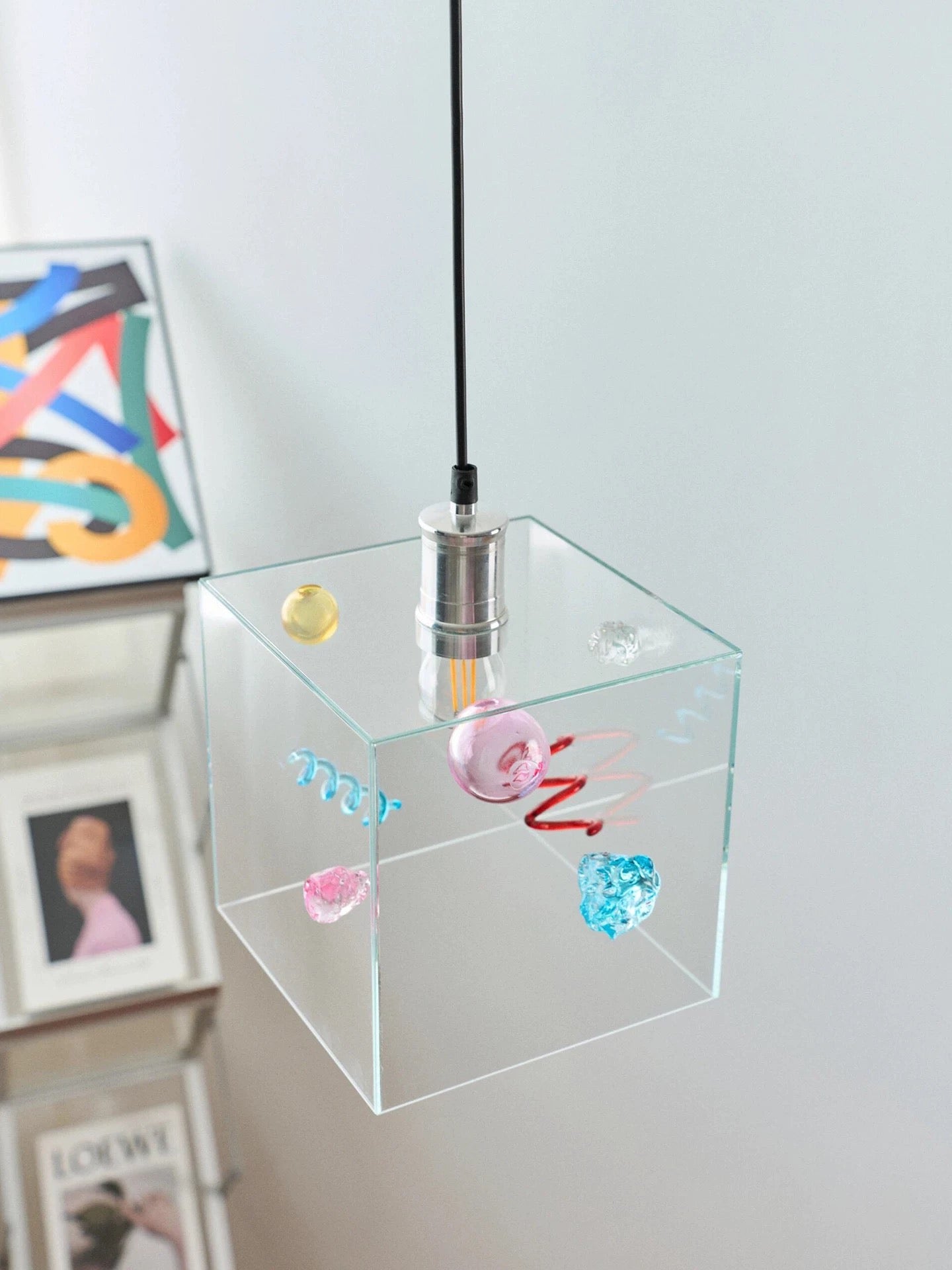 Clear glass pendant light with colorful decorations on a white wall background