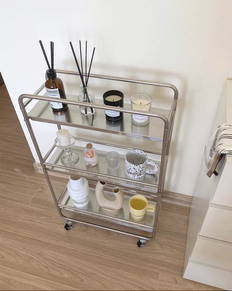 Slim chrome rolling trolley used for bathroom storage, skincare, towels, candles, and essentials.
