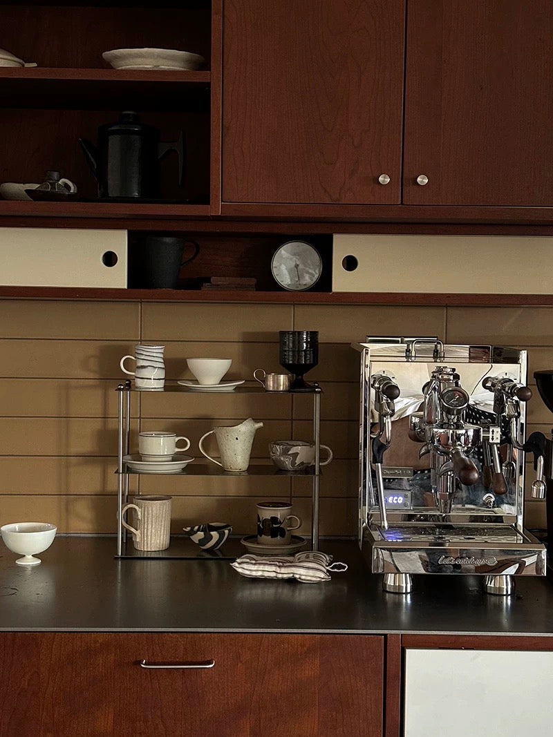 Espresso machine on a kitchen counter with shelves displaying coffee cups and a bowl.