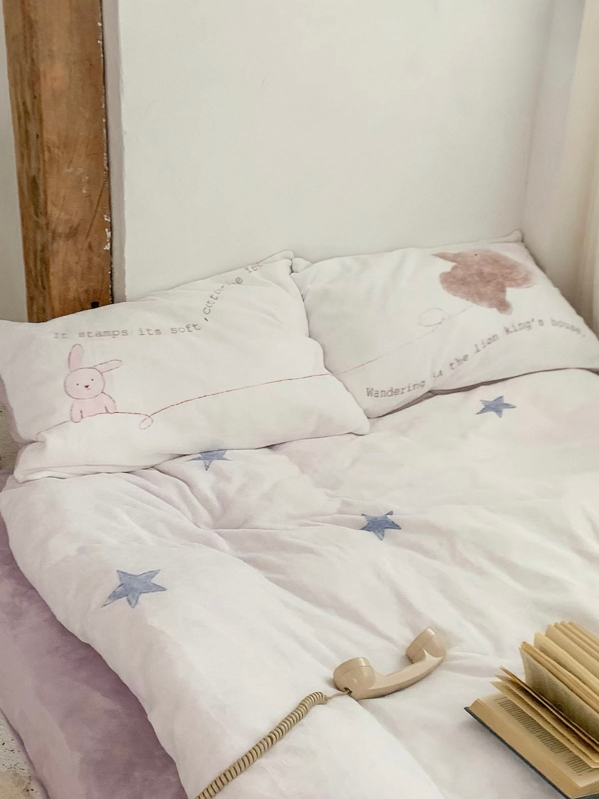 Blue stars and fine lettering cover the bed beside a telephone receiver and a stack of books.