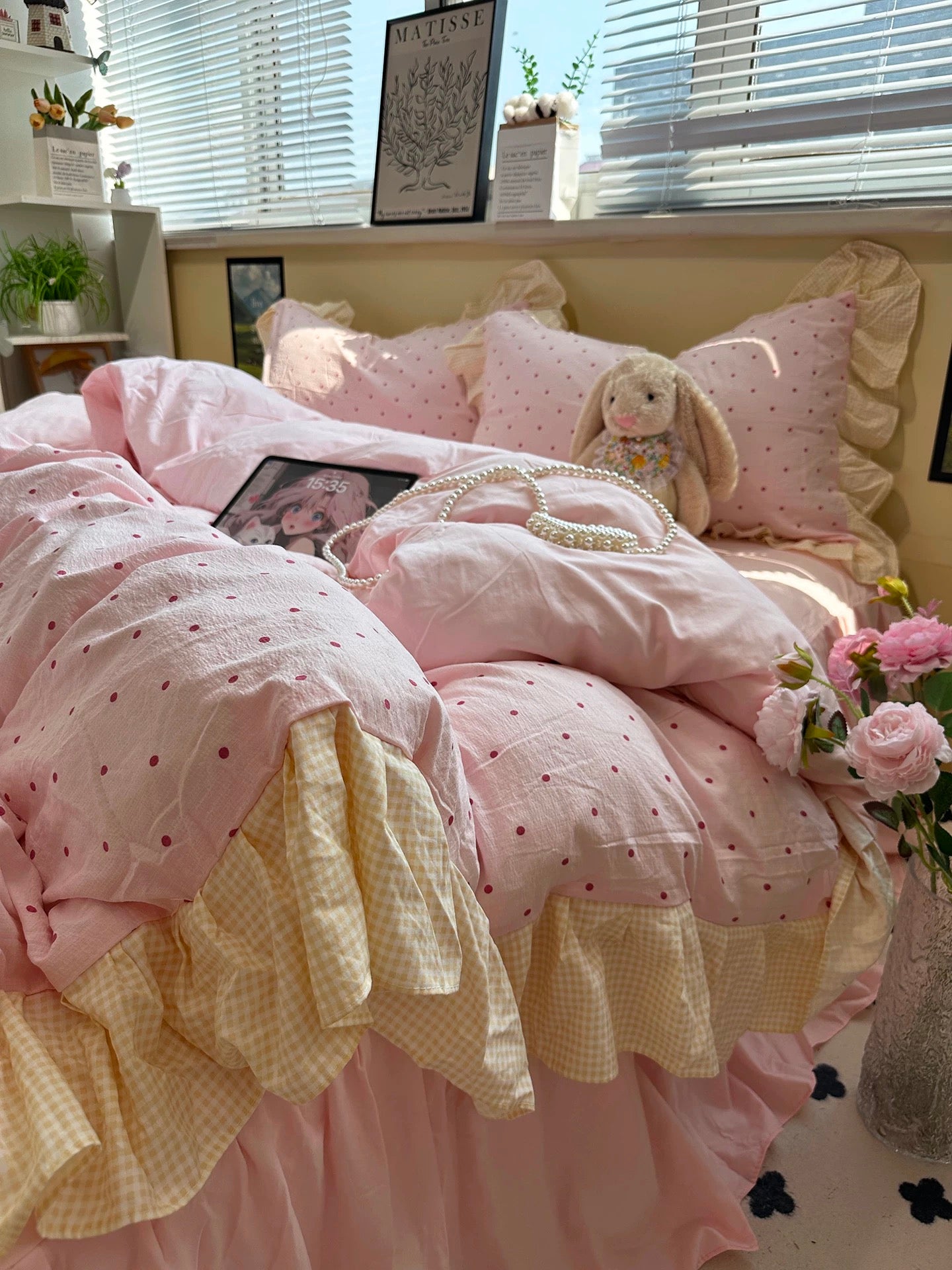 Pink polka dot bedding with a teddy bear and flowers on a bed in a bright room.