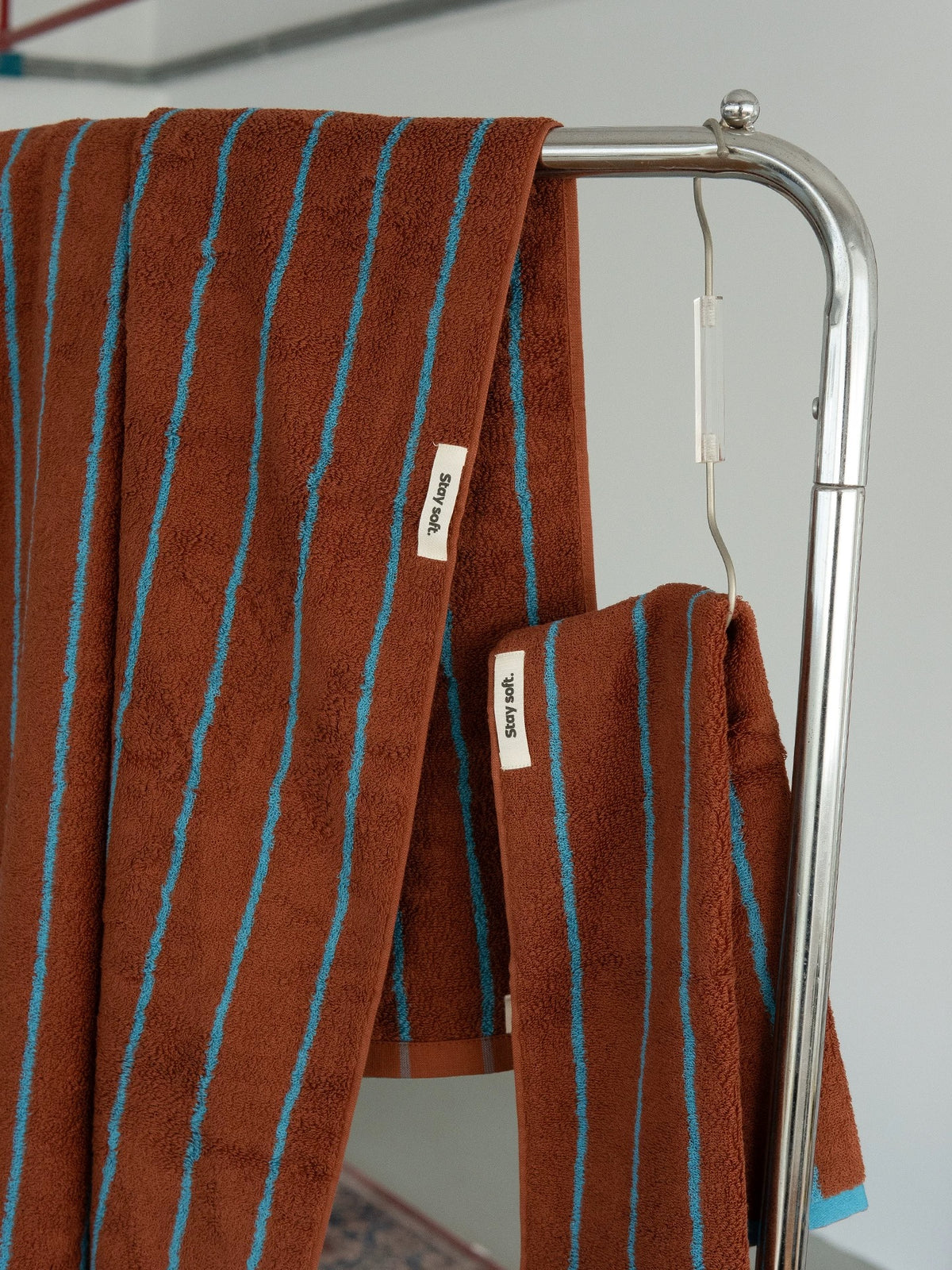 Brown towel with blue stripes hanging on a metal towel rack against a white wall.