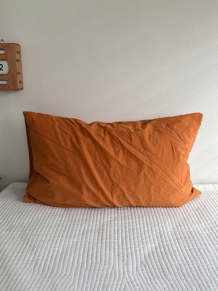 A solid orange terracotta pillowcase stands upright on white bedding.