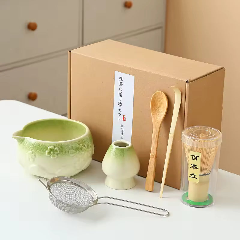 Tea-making set with green ceramic bowls, wooden spoon, and metal strainer in front of a cardboard box.