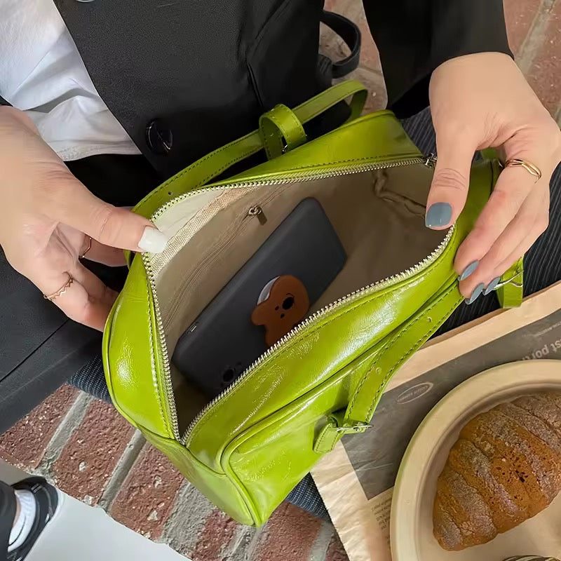 Person opening a green handbag on a brick surface