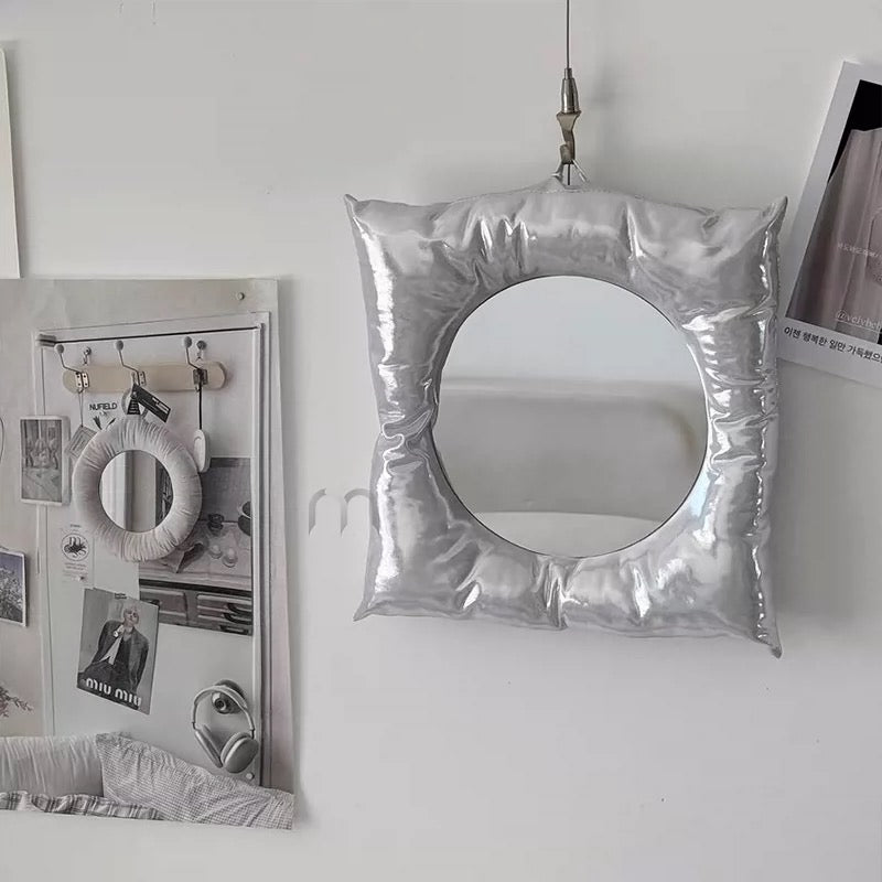 Silver inflatable mirror on a white wall with framed pictures.
