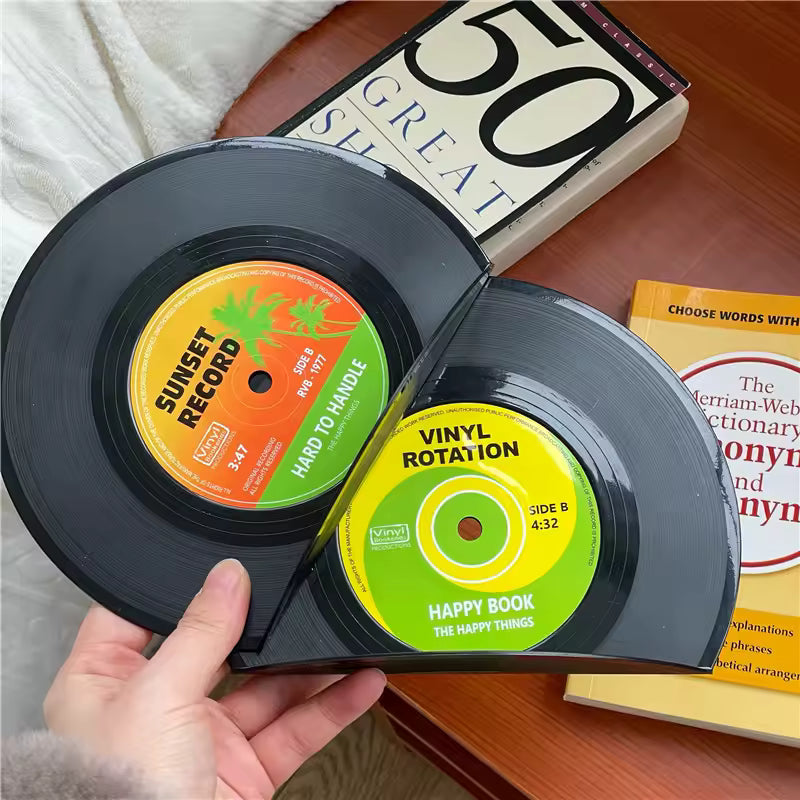 Two vinyl records with colorful labels held by a hand, with books in the background.