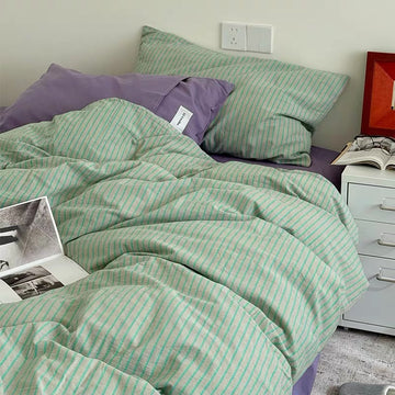 Green striped bedding on a bed with a purple pillow and open book.