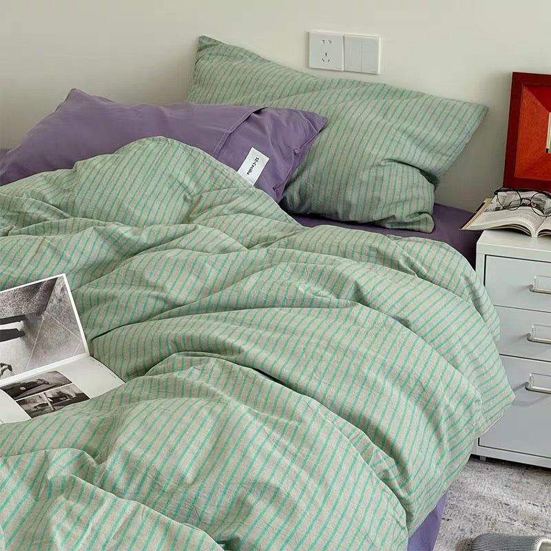 Green striped bedding on a bed with a purple pillow and open book.