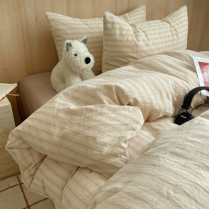 Beige striped bedding with a plush toy on a bed in a bedroom setting.