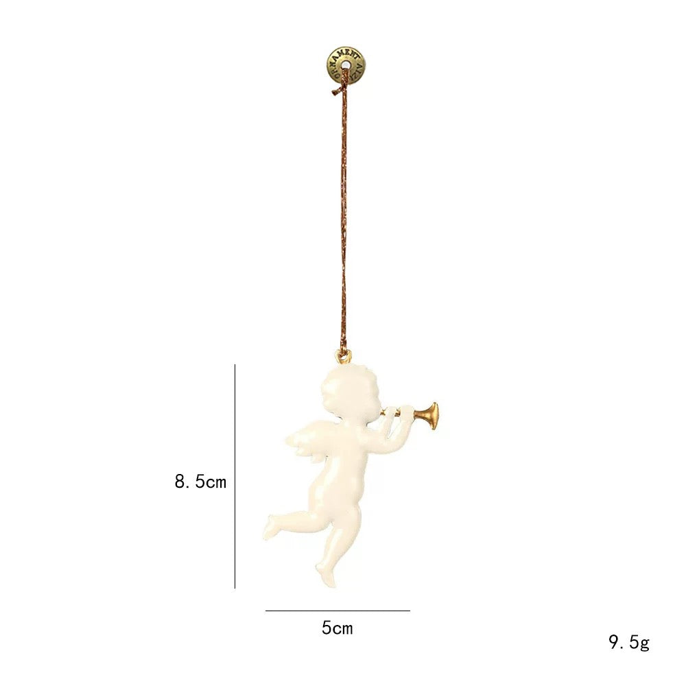 A white angel Christmas ornament holds a gold trumpet beside its face and hangs from a gold colored cord.