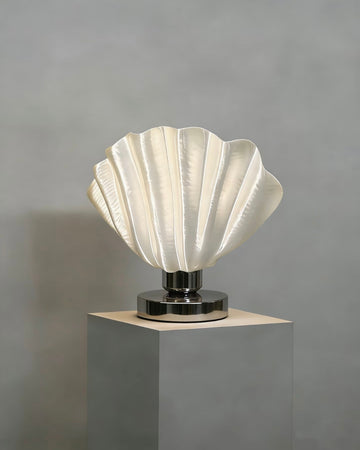 White scallop table lamp with shell relief design on bedside table creating soft warm ambient light