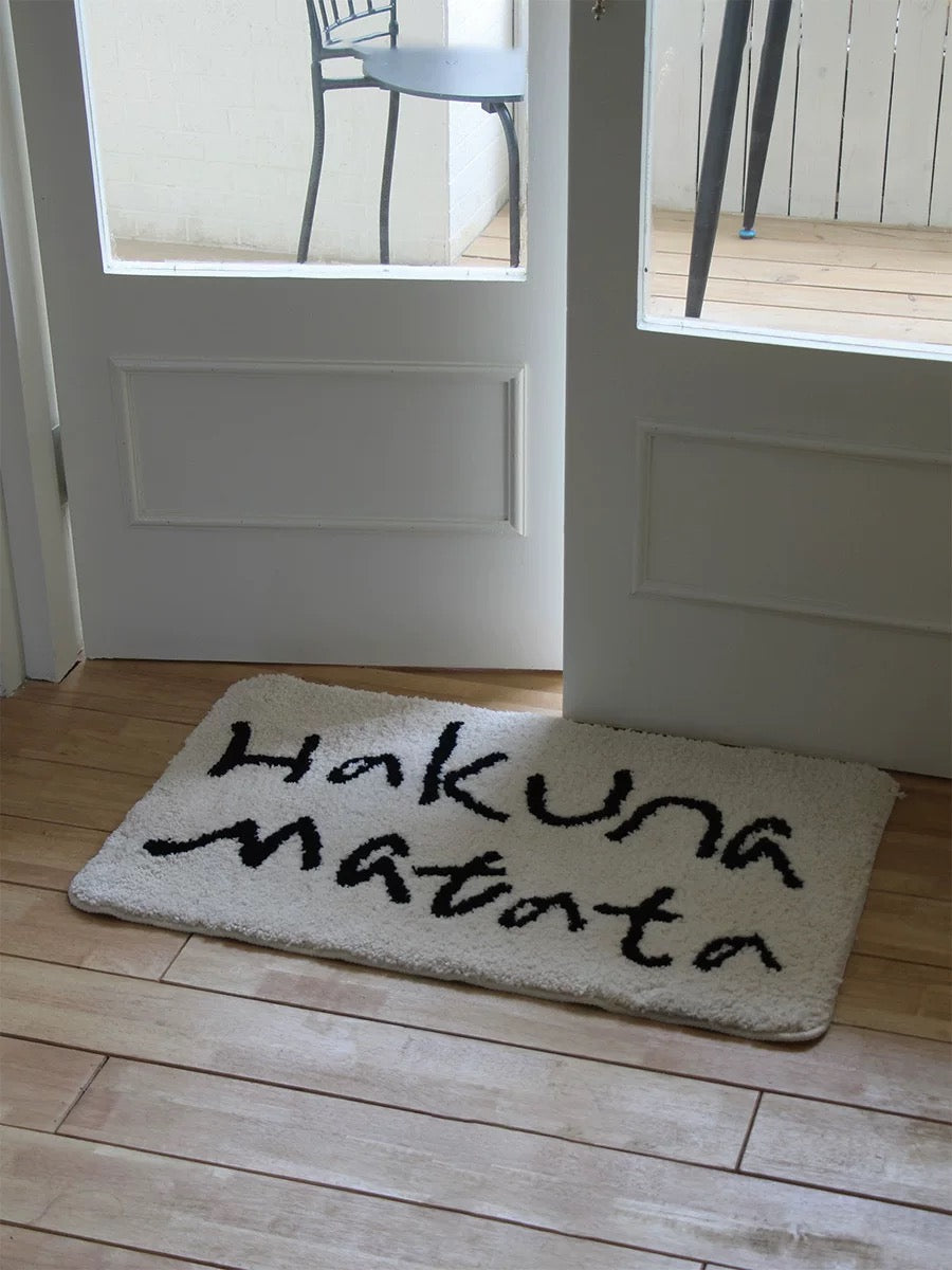 A white slogan bath mat sits across a doorway, with two rows of black lettering facing into the room.