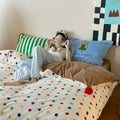 Person lying on a bed with colorful bedding and pillows, holding a teddy bear.