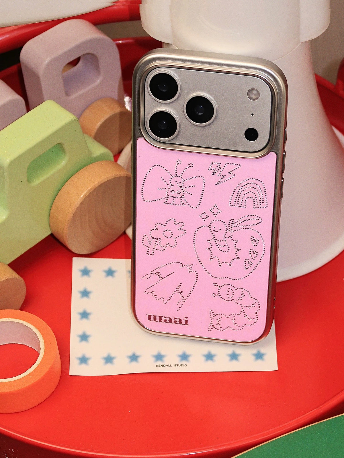 A pink Y2K phone case shown close up, with its silver butterfly and cartoon apple illustrations visible.