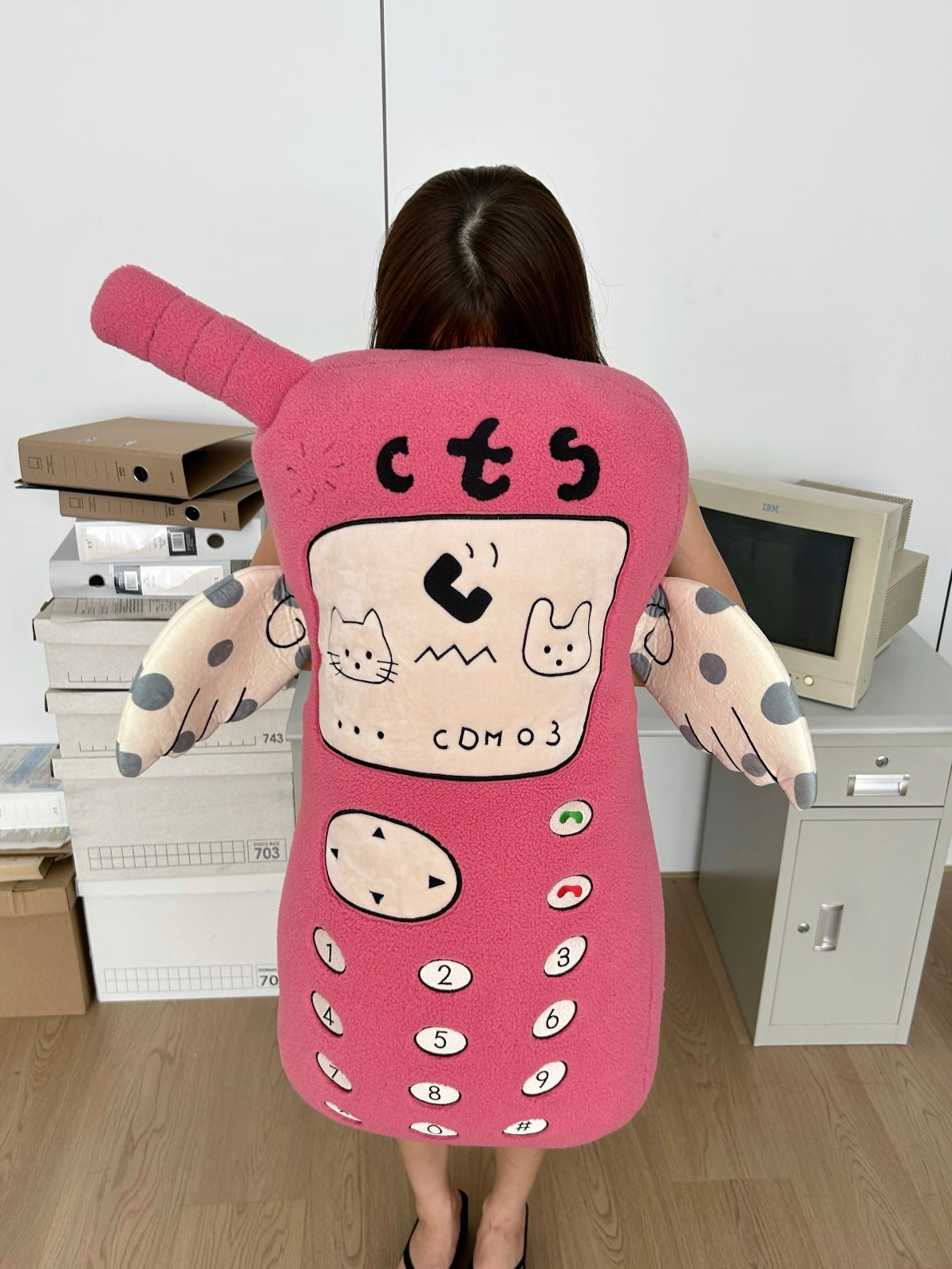 A pink phone Y2K pillow faces forward, with a raised antenna, embroidered screen details and pale spotted arms.