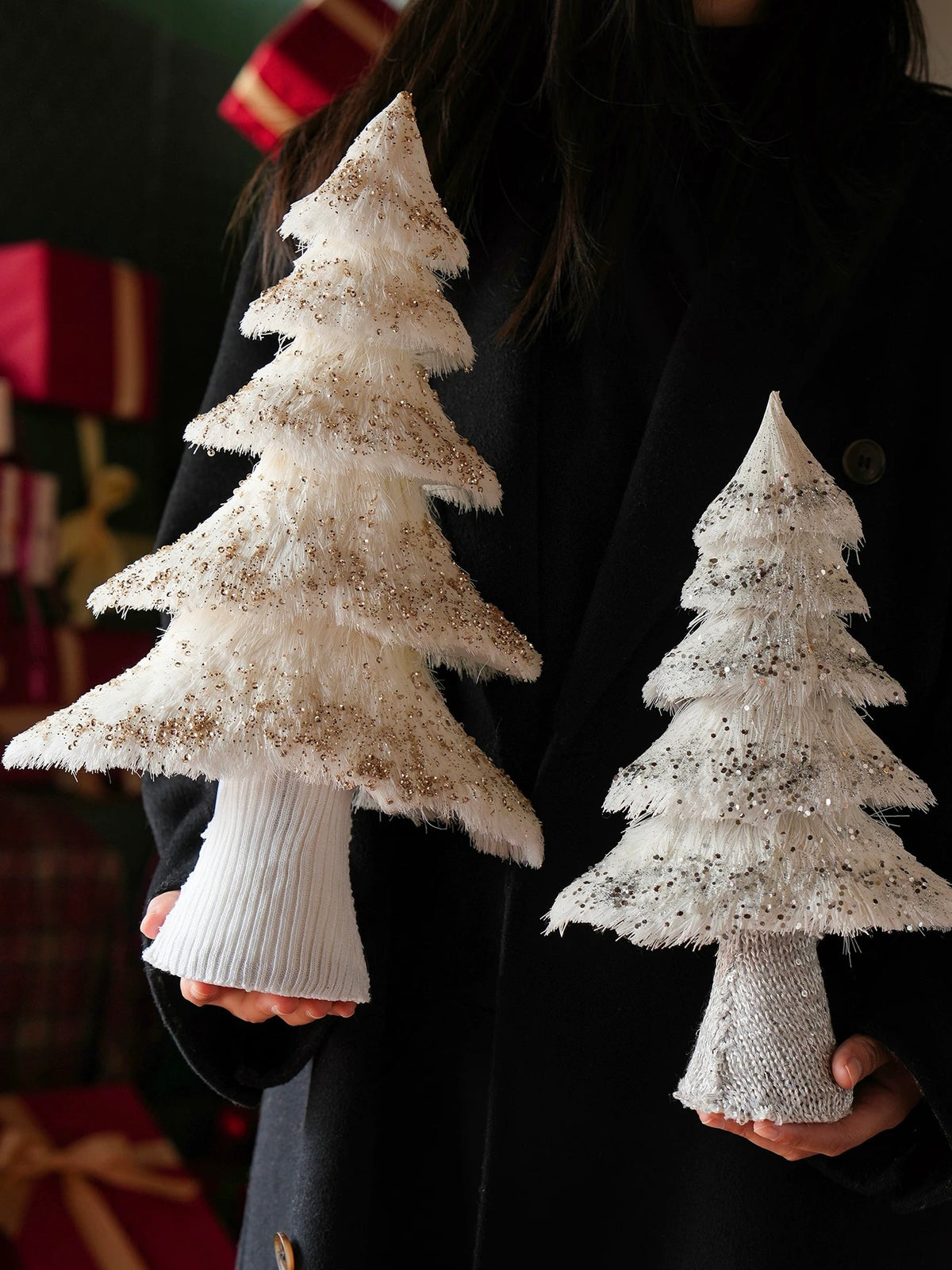 Two yarn Christmas tree decorations are held side by side, showing their tapered tops and layered branch edges.