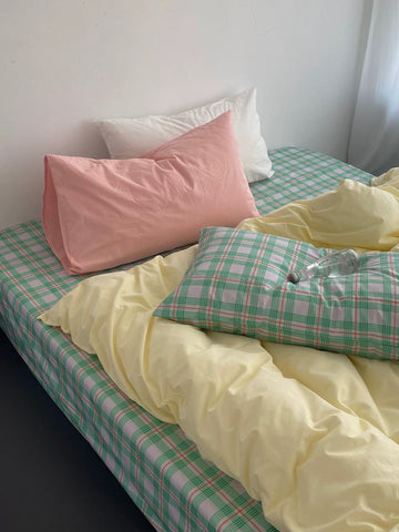 Bed with checkered green and pink sheets and pillows in various colors.