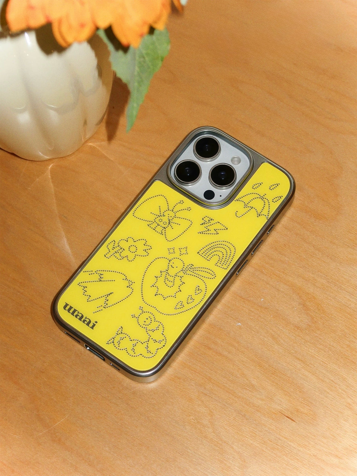 A yellow butterfly phone case viewed from above, with a rainbow and cartoon apple among the silver drawings.