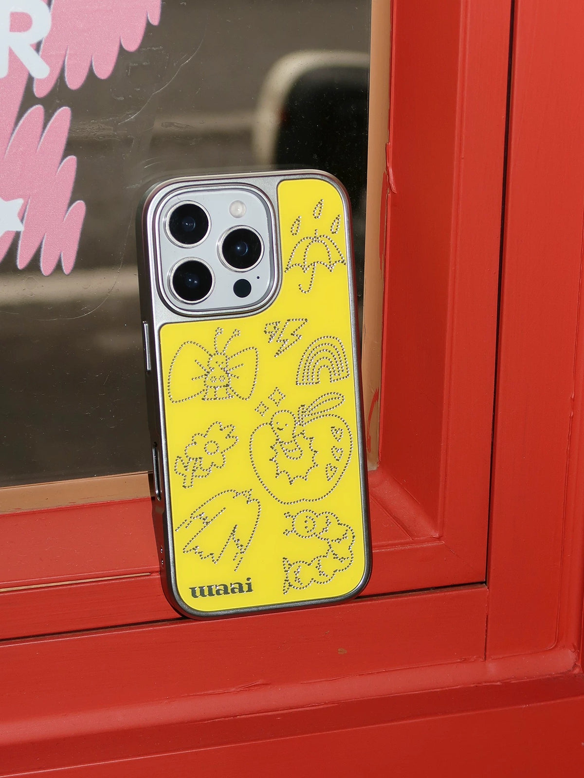 A yellow doodle phone case standing upright, showing the silver border around the back and camera opening.
