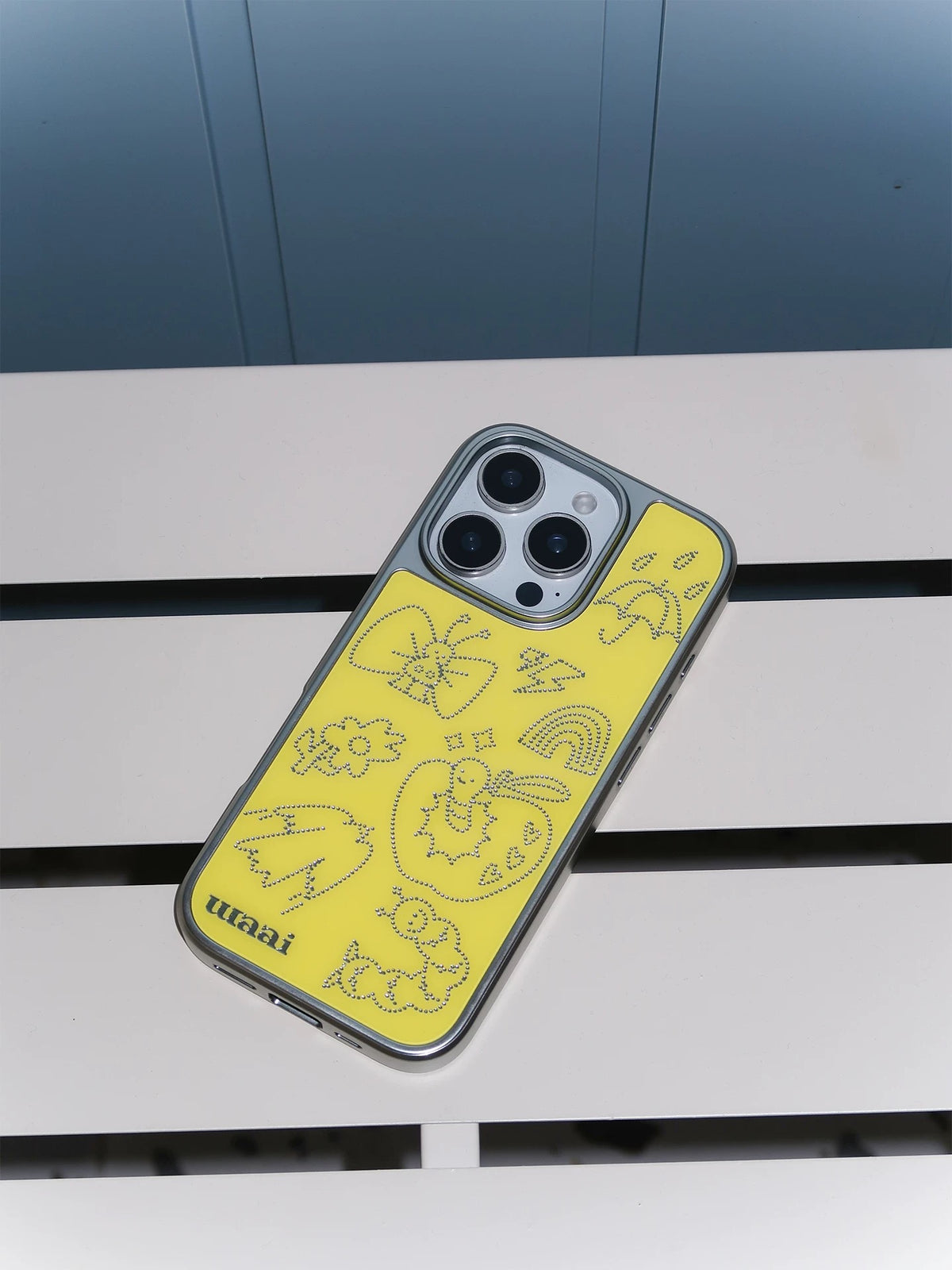 A yellow iPhone case tilted at an angle, with the silver butterfly, apple and candy artwork facing up.